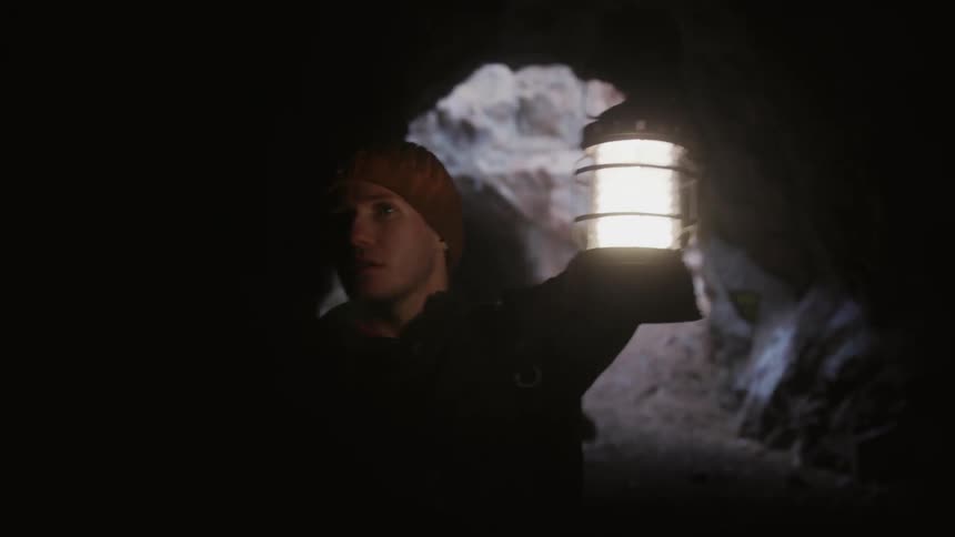 A man carries a lantern and looks around a cave
