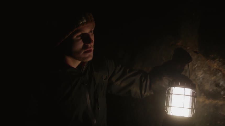 A man explores a cave holding a lantern