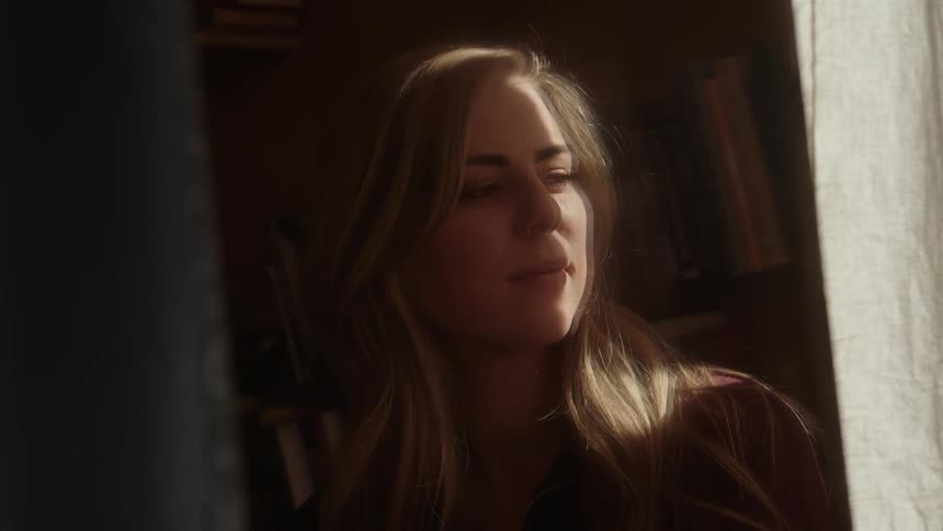 A woman standing near bookcases looks into the sunlight