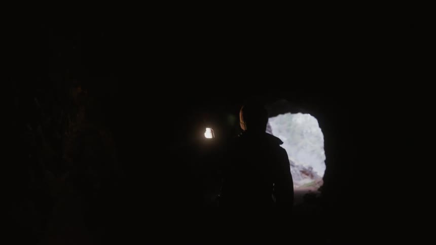 Man holding lantern is walking through dark cave