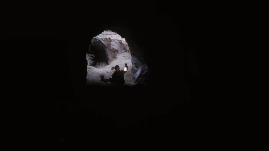 A man holding a lantern walks into a cave