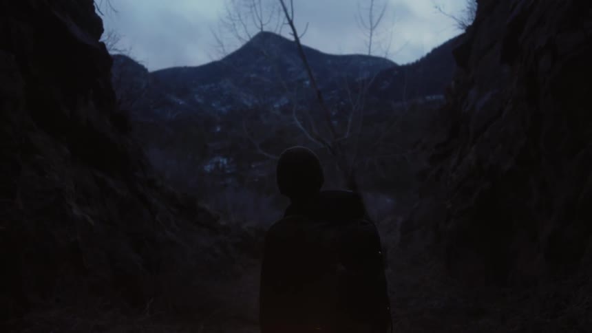 Person stands in the mouth of a cave on a cloudy day