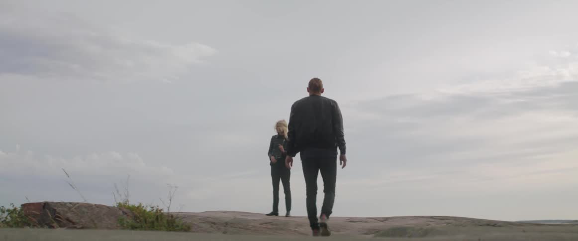 An anxious young male steps toward a lonely blonde female standing outside alone.
