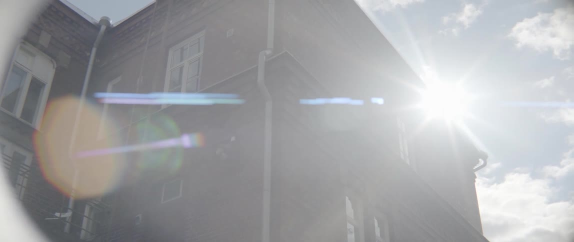 Bright summer sunlight shines down intensely creating a lens flare on brick building.