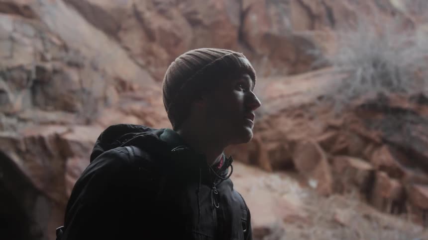A man is looking up at the cliffs around him and then walking on in daylight