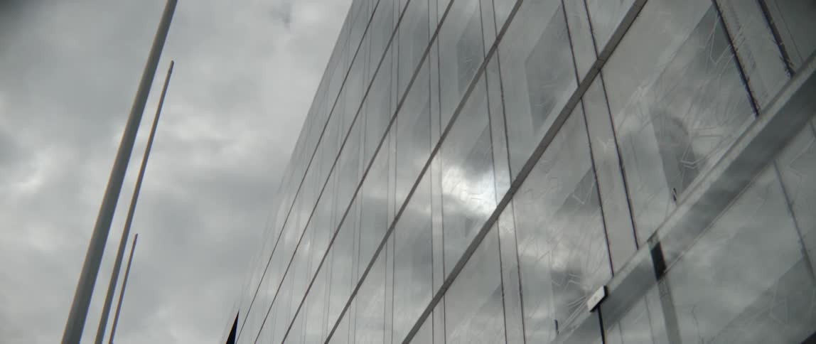 Shiny glass facades on a contemporary skyscraper reflect grey stormy weather during daytime.