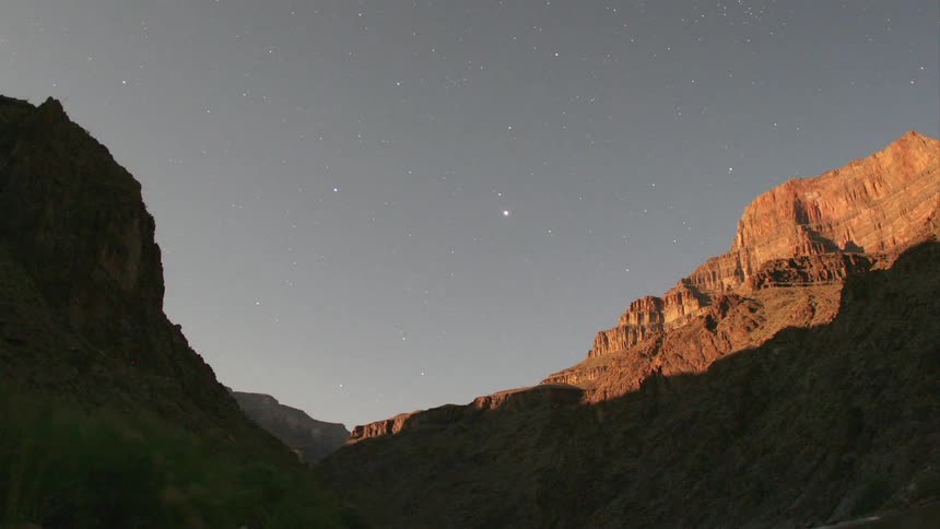 Stars fill the sky as day turns to night above a canyon
