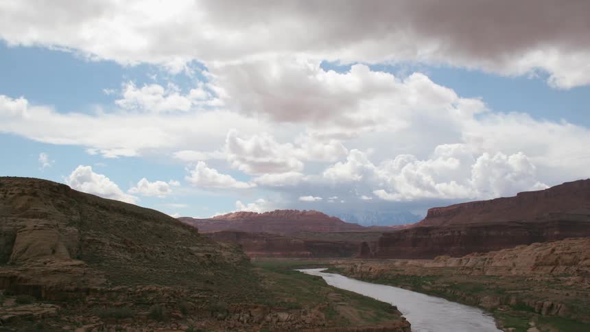 Time lapse of a canyon with a calm river flowing and large billowing clouds in the sky