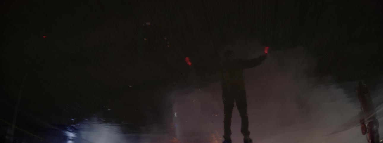An airport worker with flares is reflected on the wet surface of a runway