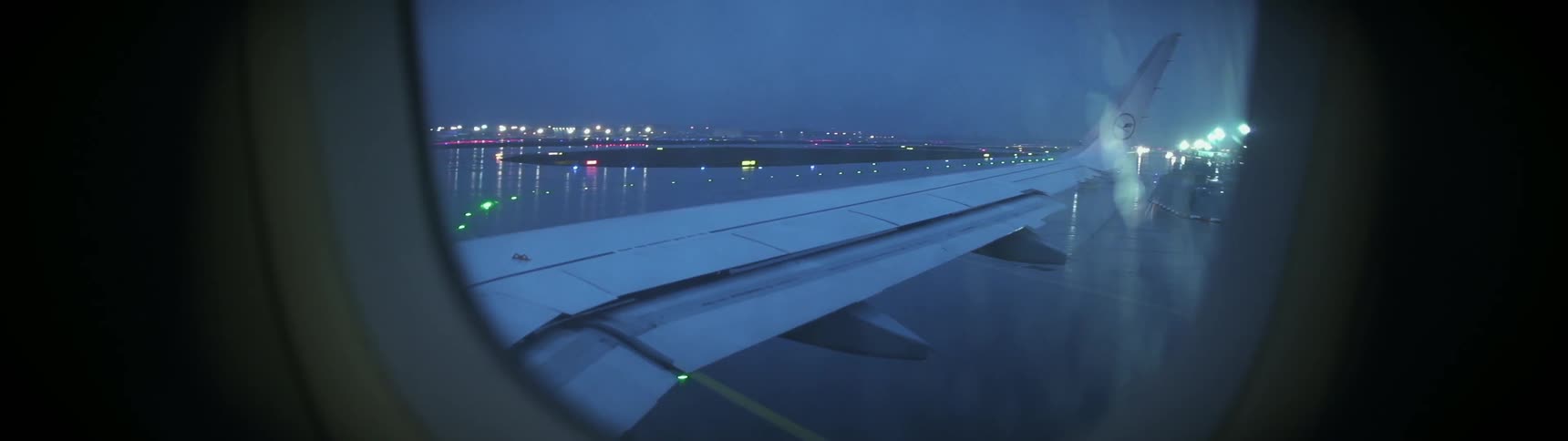 An airplane is taxiing down a runway at an airport on a rainy night