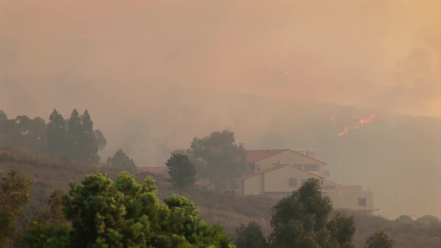 Helicopter moves overhead into a smokey sky above a house on a hill