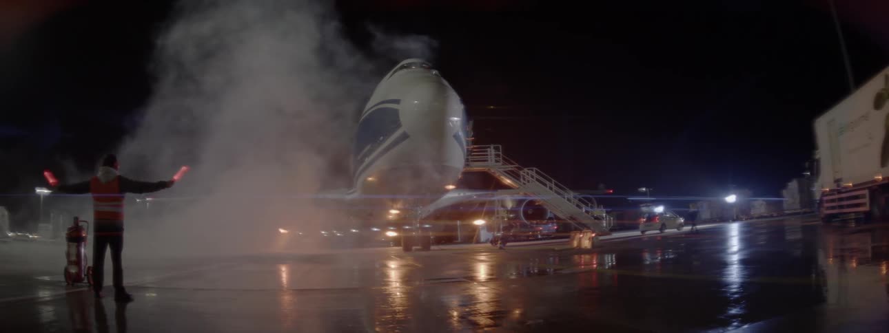 A worker on the tarmac waves light sticks in front of a plane