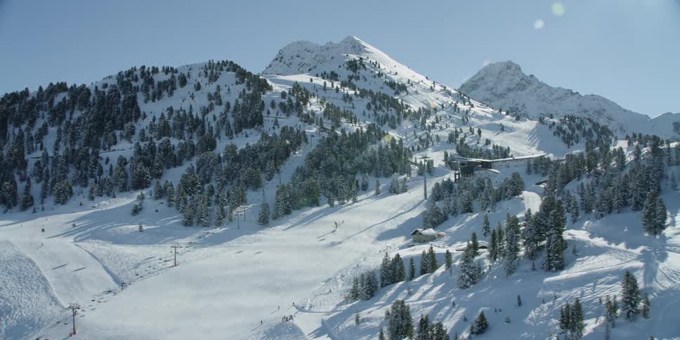 Snow and pines trees cover mountains on a sunny day