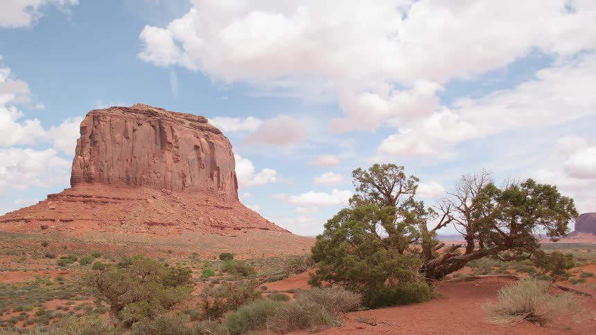 White clouds in a bright blue sky move over a red rock formation in the desert