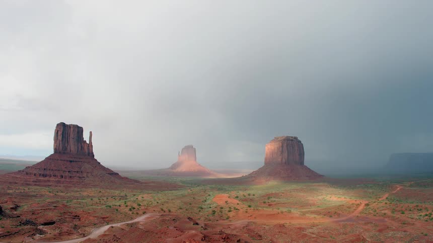 Vehicles drive down a winding narrow road near canyons as a rainbow fades in the background