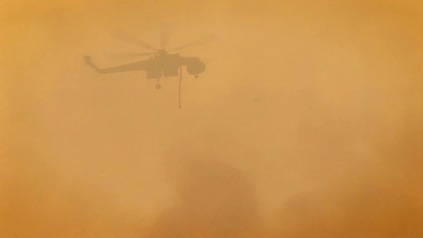 Large helicopter travels over a smokey area and drops huge amounts of water