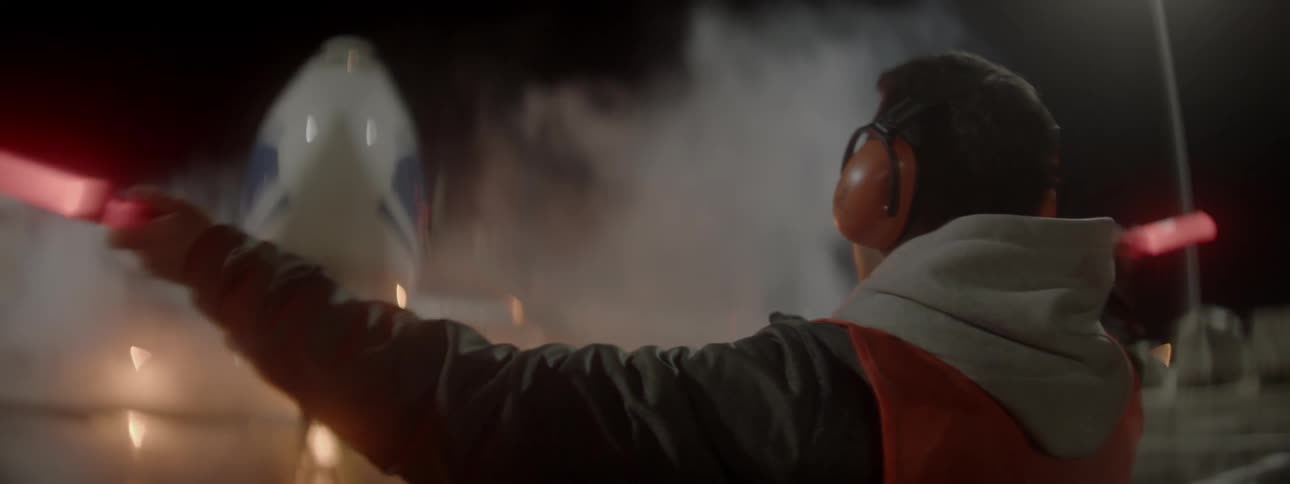 Man wearing earphones waves glow sticks for a landing airplane at night