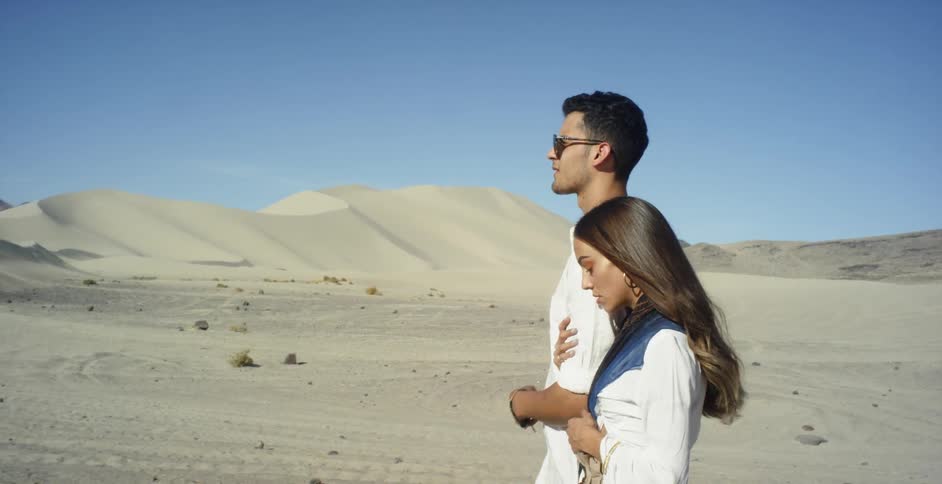 A woman is holding onto a man's arm as they walk in the desert on a sunny day