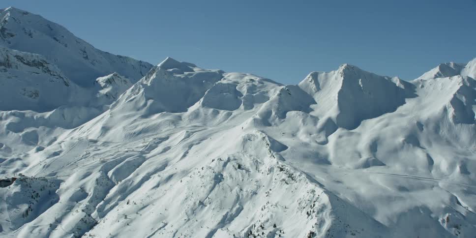 Snow is covering the slopes of a mountain range and valley during the day