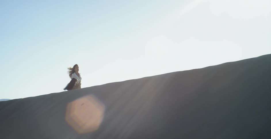 A woman is running along the top of a sand dune on a sunny day