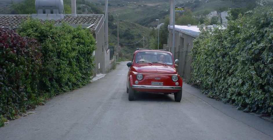 A couple are driving in a car in a rural european village in daylight