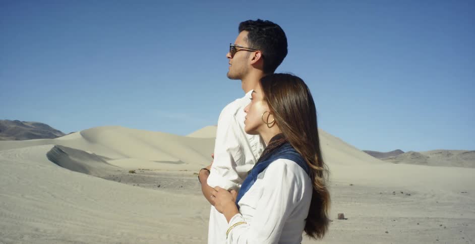 Man and woman walking together near sand dunes on sunny day