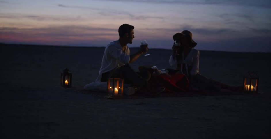 Man and woman drink out of glasses in the sand on the beach
