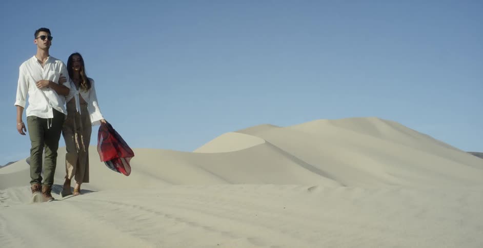 Man and woman walk in a hilly desert on a clear day