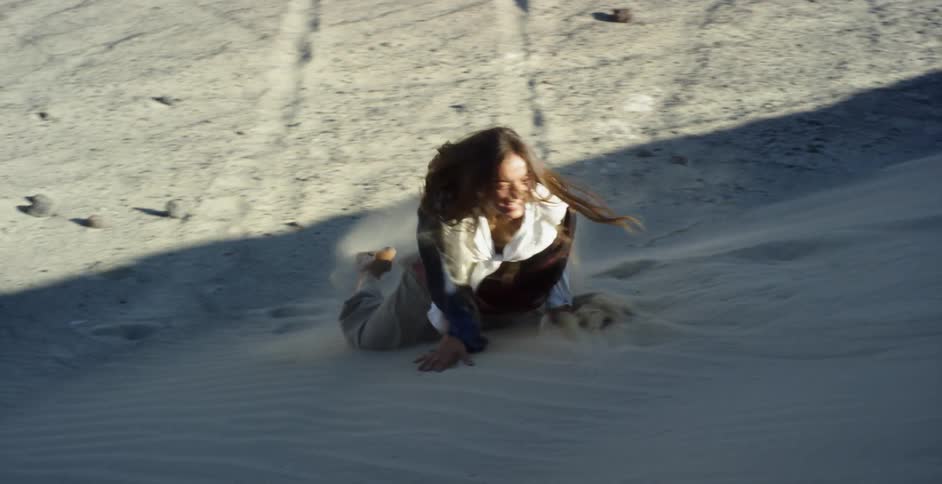 A woman laughs as she rolls down the sand hill
