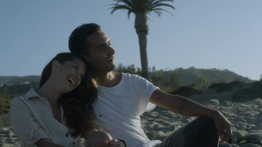 A woman rests her head on her boyfriend's shoulder on the beach