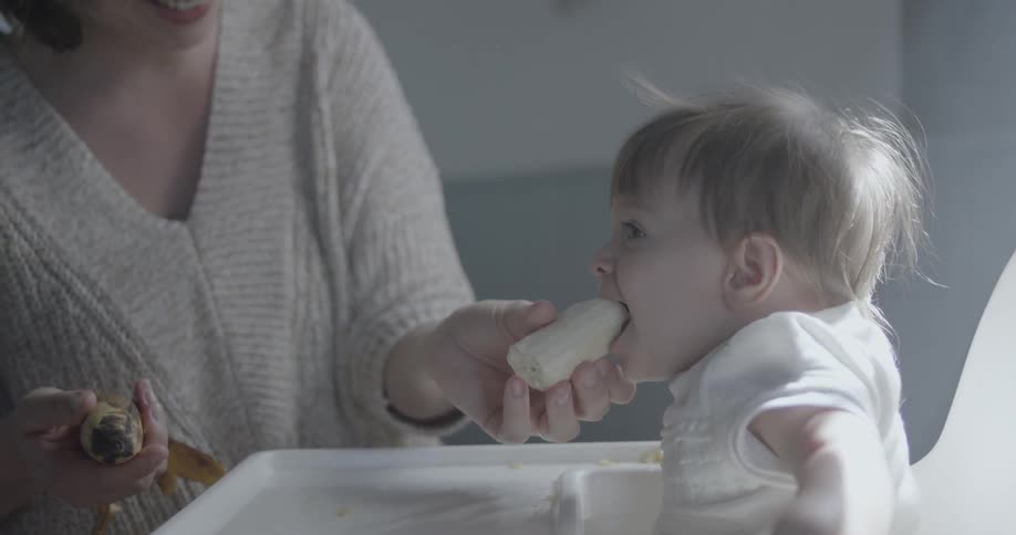 Woman feeds banana to a baby