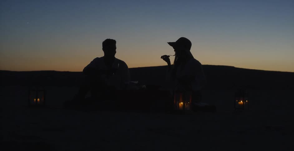 A man and woman dine together on the beach at sunset