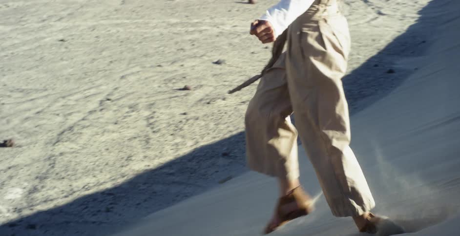 Woman in brown pants and white shirt runs down a desert dune