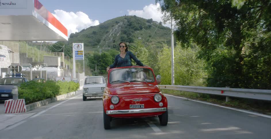 Woman stands and looks out over the roof of a moving car