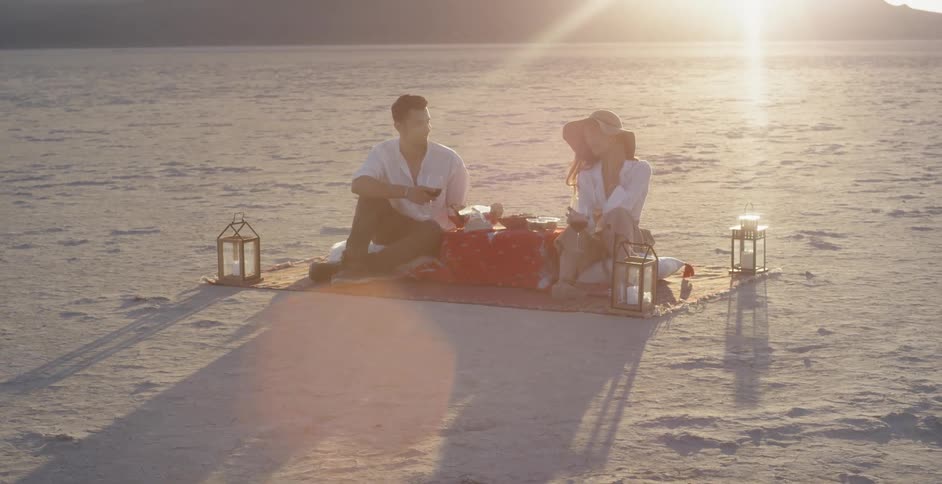 Man and woman having picnic in sand as sun sets