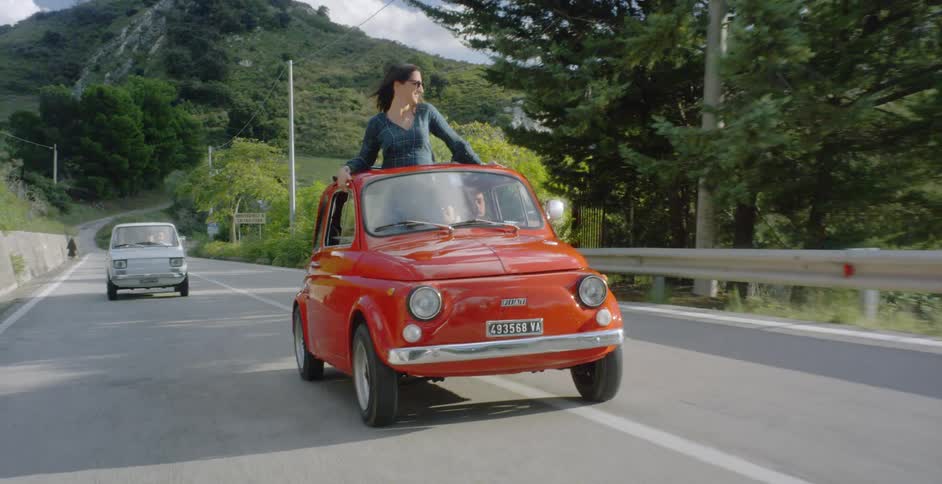 Woman standing in a car without a roof down a country road