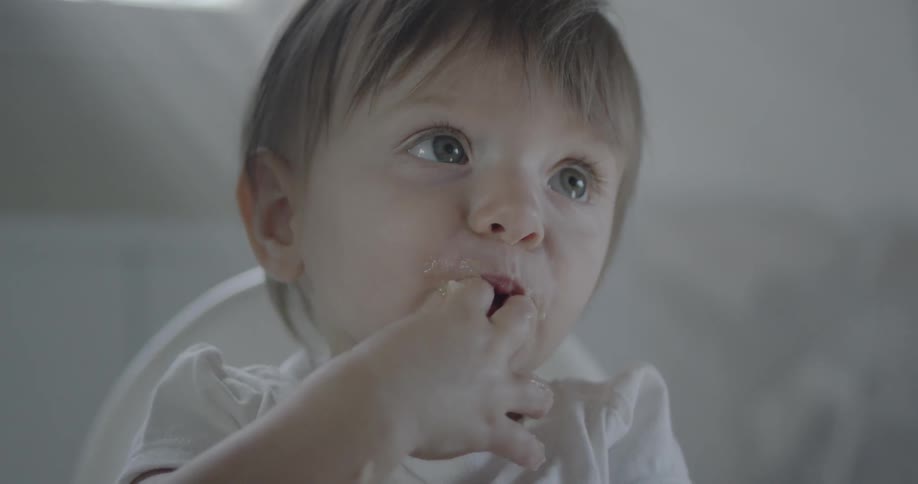 A baby is eating and laughing as he sits in a highchair