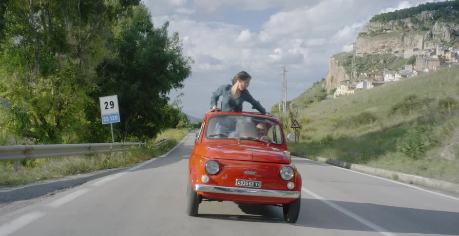 Woman standing in a car without a roof down a country road