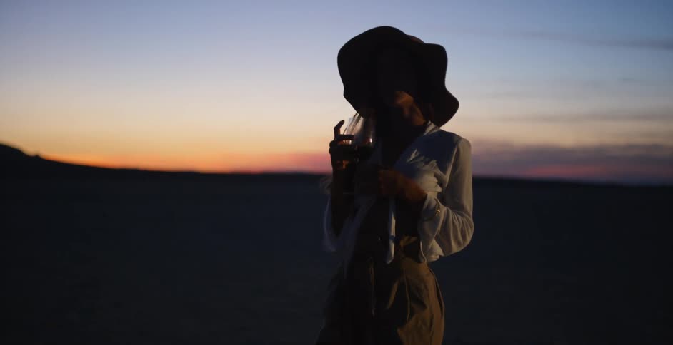 A woman is drinking a glass of wine in the desert at sunset