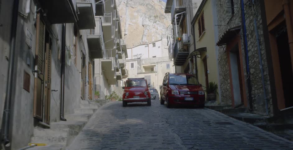 Cars travel on a cobblestone road in a village