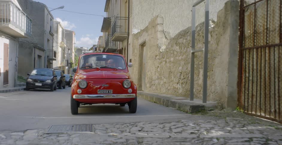 A couple are driving in a car through an old world village on a sunny day