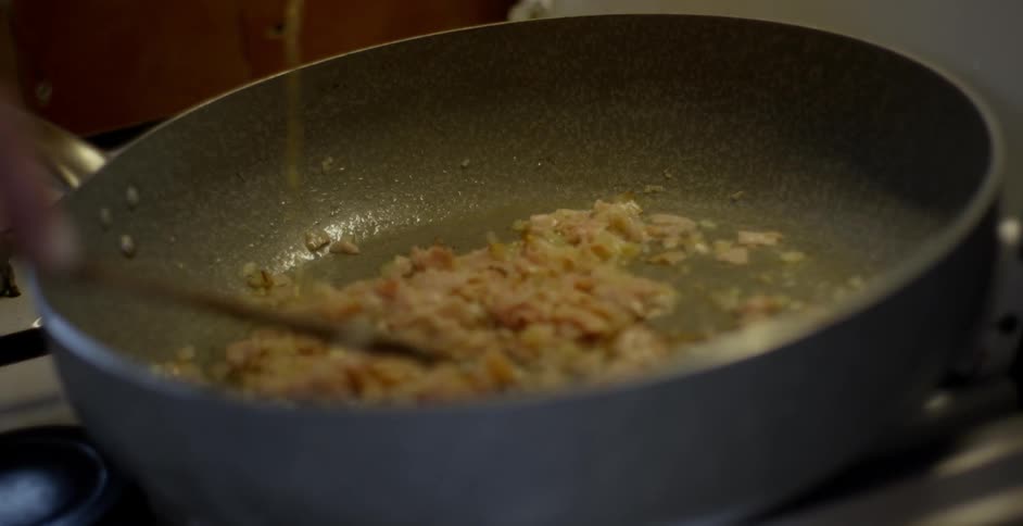 Person pours liquor into a pan of food and stirs in the pan