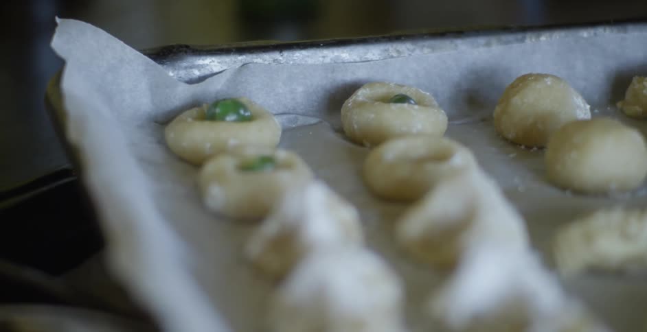 A baker adds a piece of fruit to the cookies on a tray