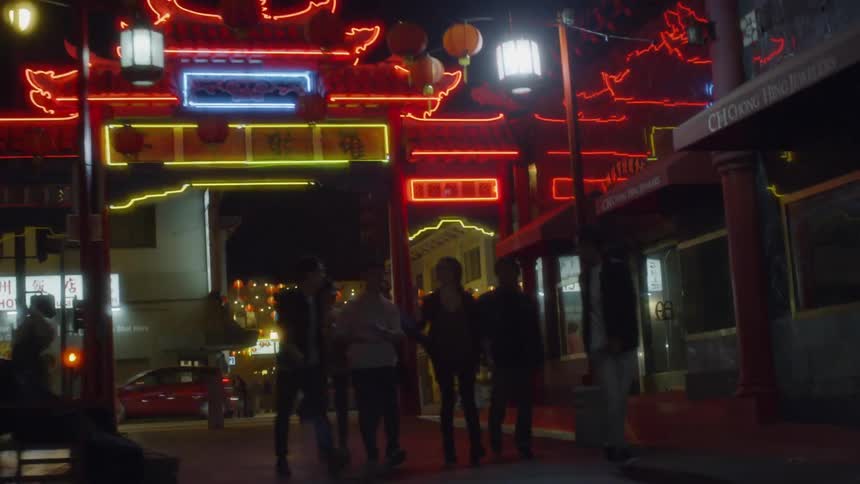 Group of people walk down an alleyway with neon lights overhead