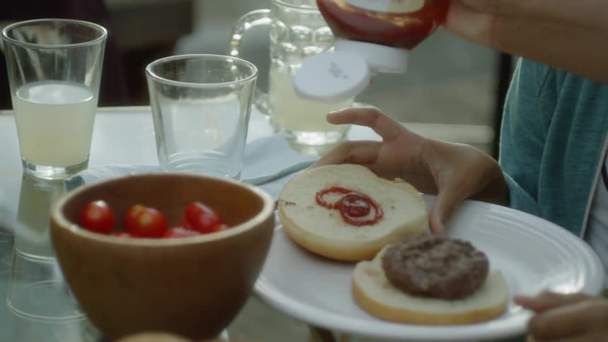 Person squeezes ketchup onto a burger bun