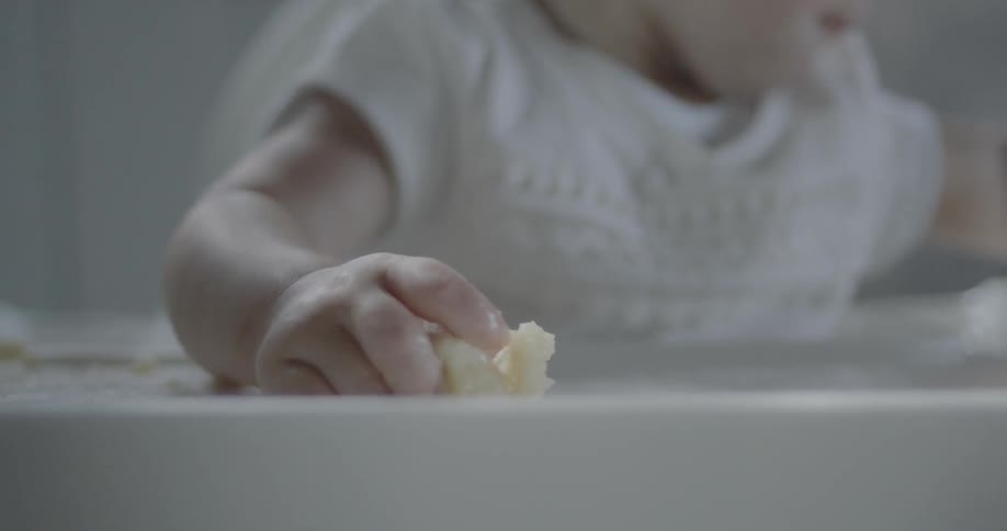 A baby is eating and playing with his food as he sits in a highchair
