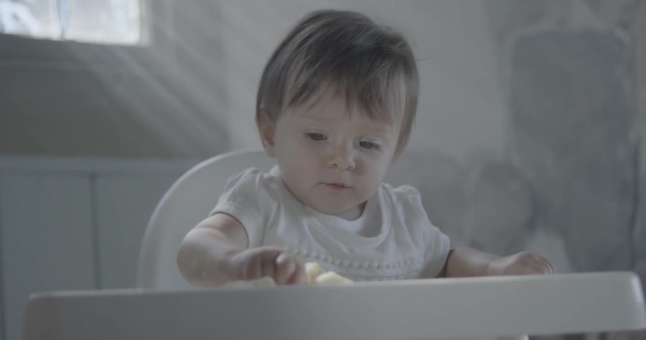 Baby eats banana in a highchair