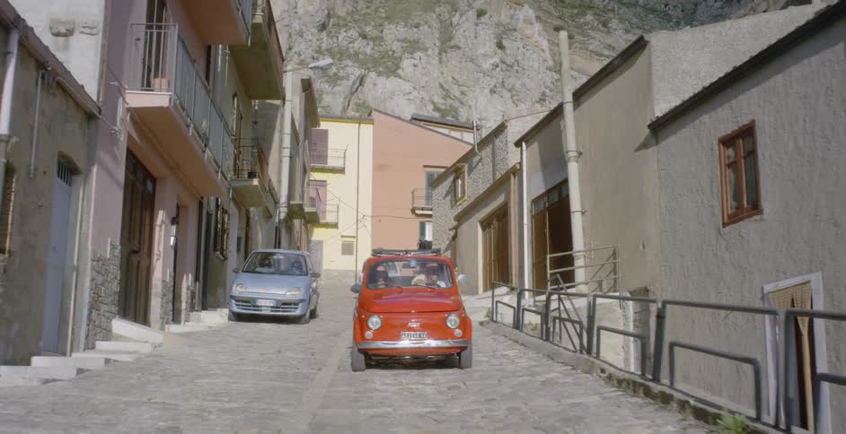 A car travels down a cobblestone village road