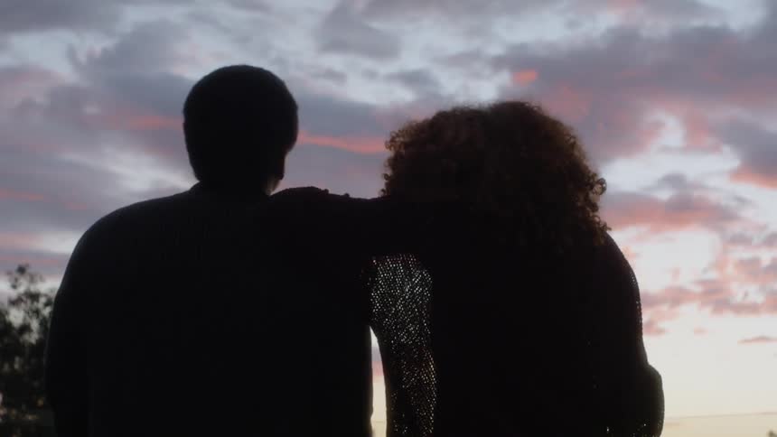 Man and woman stand outside with arms around each other at sunset