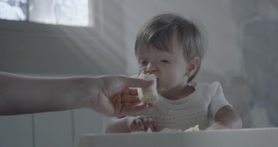 A child is being fed a banana in a high chair